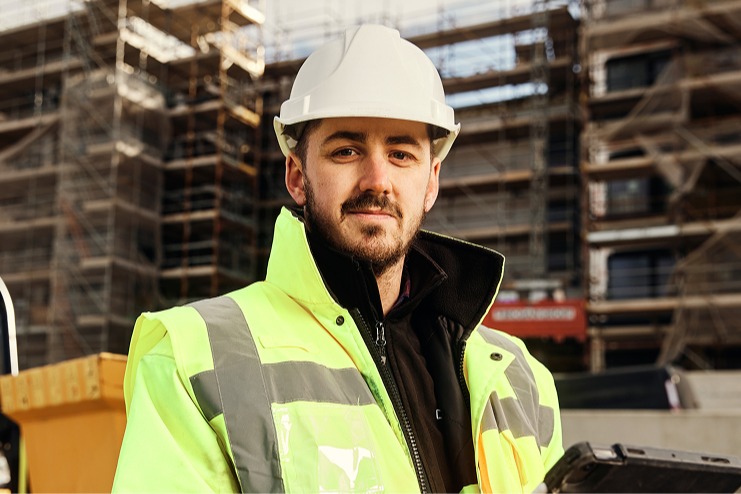 Construction worker in a white helmet and yellow jacket at site.