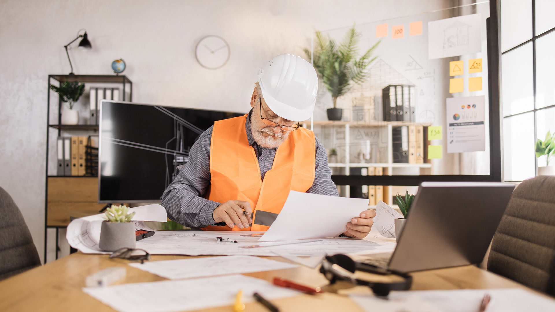 a person wearing a hard hat and orange vest sitting in a desk looking at papers