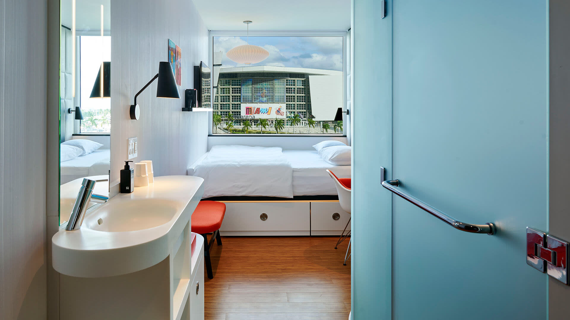 A room with a bed, sink and a window looking at a stadium