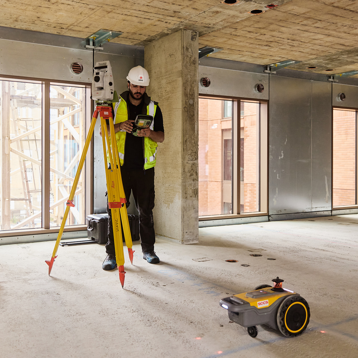 A construction worker operating a total station alongside a robot. 