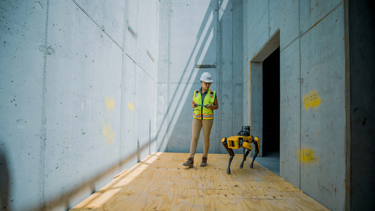 A woman in a safety vest and a helmet standing in a room with a robot