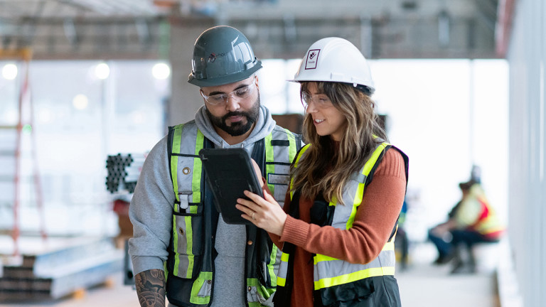 Two construction workers having a conversion while using a tablet