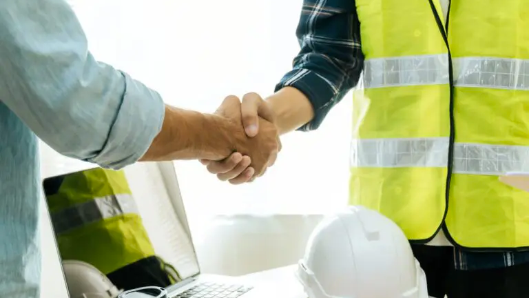 two workers one dressed in PPE shaking hands over a desk