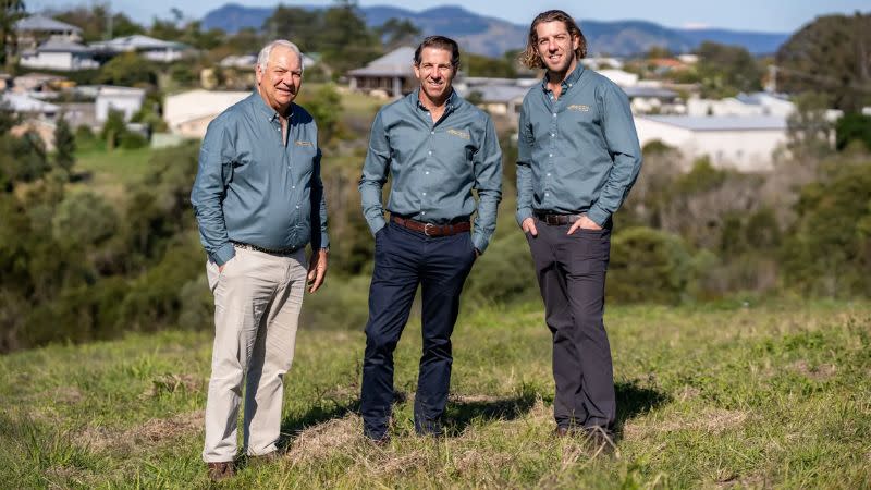 three men standing on a block of land in green shirts and casual pants
