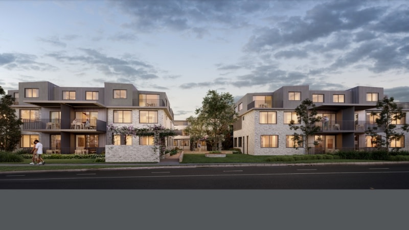 the low density apartment buildings at dusk showing people walking around the site and illuminated windows.