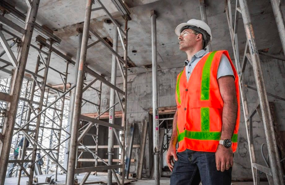 A man in a high vis vest looks up at the steel frame of a building under construction. The City of Melbourne has announced a new code of practice for construction, building and works.