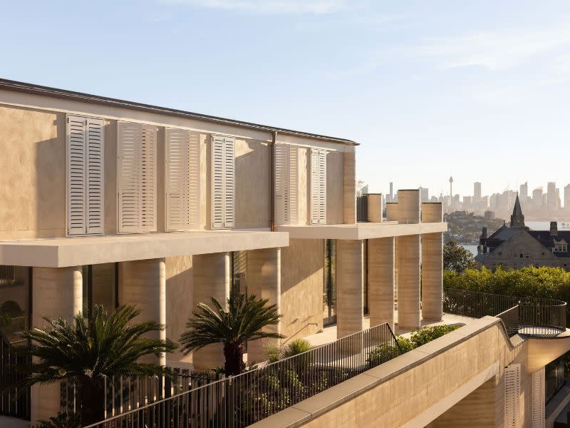 Photo showing columns along the side of the house with church-like structure in background, then city skyline over the harbour.