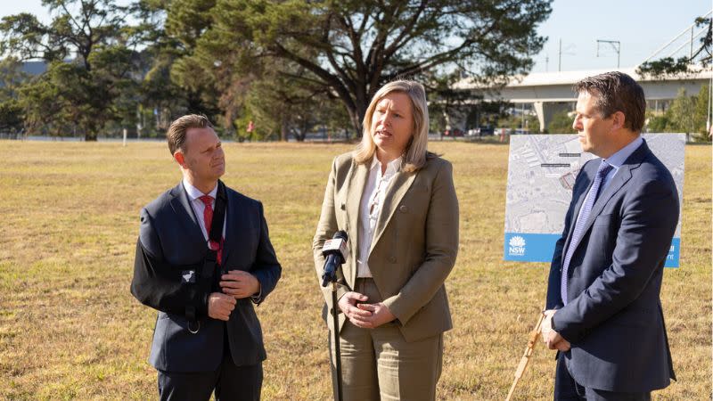 Three people discuss plans for Rouse Hill Hospital Campus on a spare block of land next to the Sydney Metro bridge.