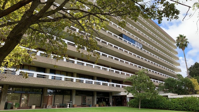 the outside of a 1970s care facility in adelaide with brown brick and white balustrades on green lawns.