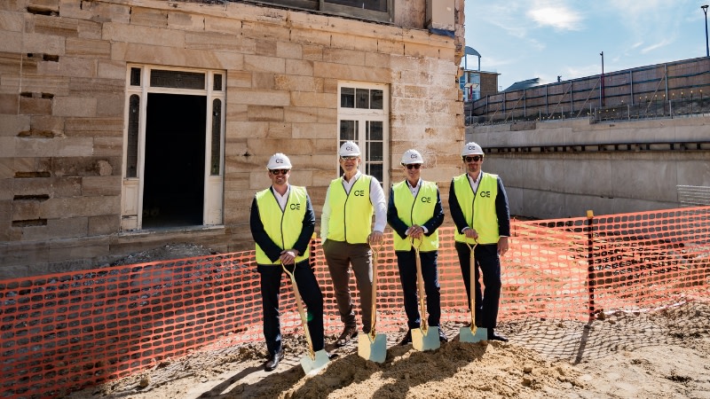 four men in high-vis vests over suits stand with golden shovels in front of Ballamac House in Coogee. 