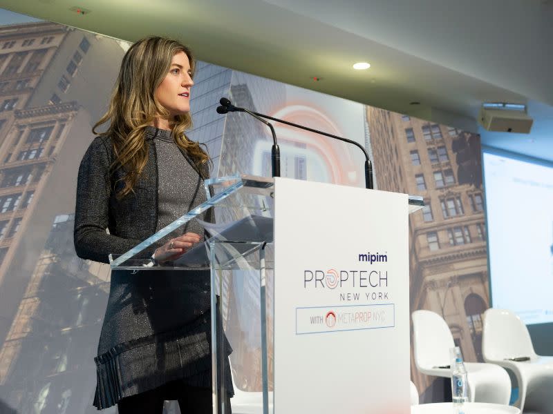 Nikki Greenberg on stage in New York standing behind a clear podium and talking to a large audience on the future of property.