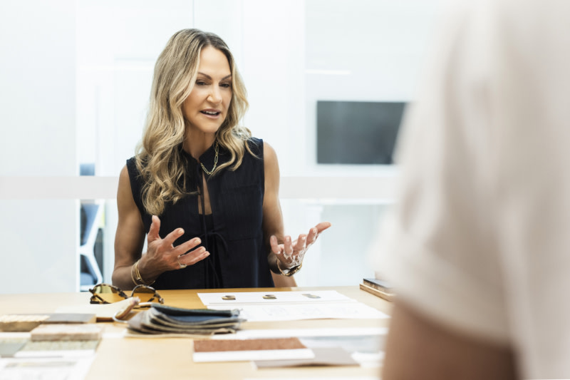 A blonde woman gesticulates while sitting at a table at a business meeting discussing the interior design of The Mondrian Gold Coast hotel.