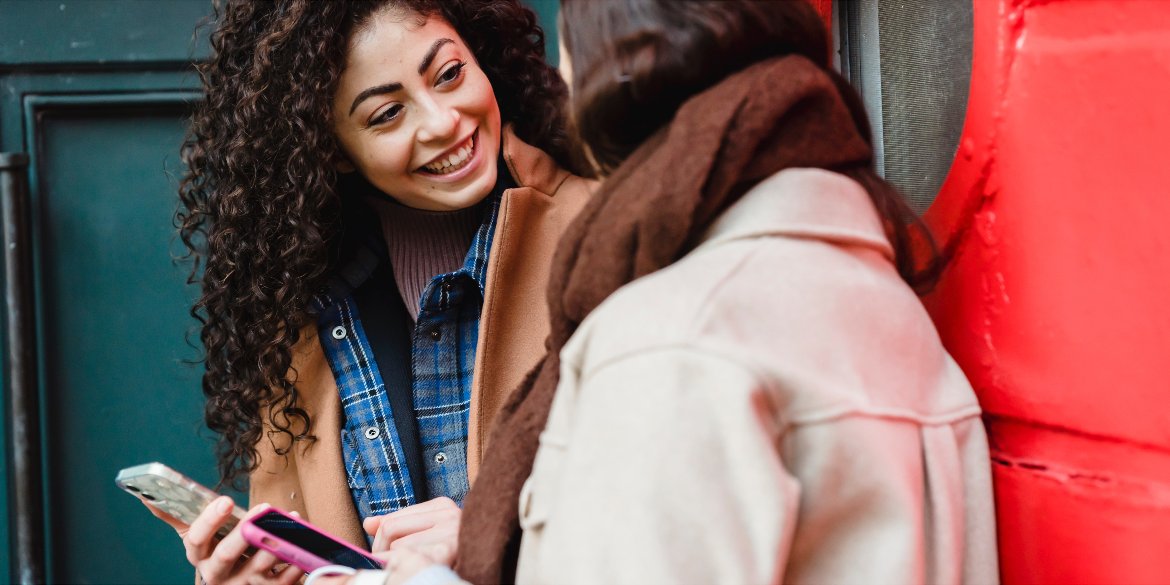 Two people having a conversation. They both have mobile phones and one of them is smiling.