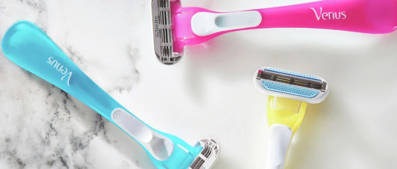 Three Venus Disposable razors in various colors on a marble surface, showcasing women's shaving products.