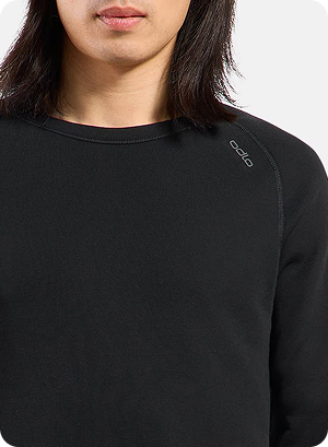 Close-up of a person wearing a black crew-neck base layer top with small “odlo” logo on the shoulder, long dark hair visible against white background.