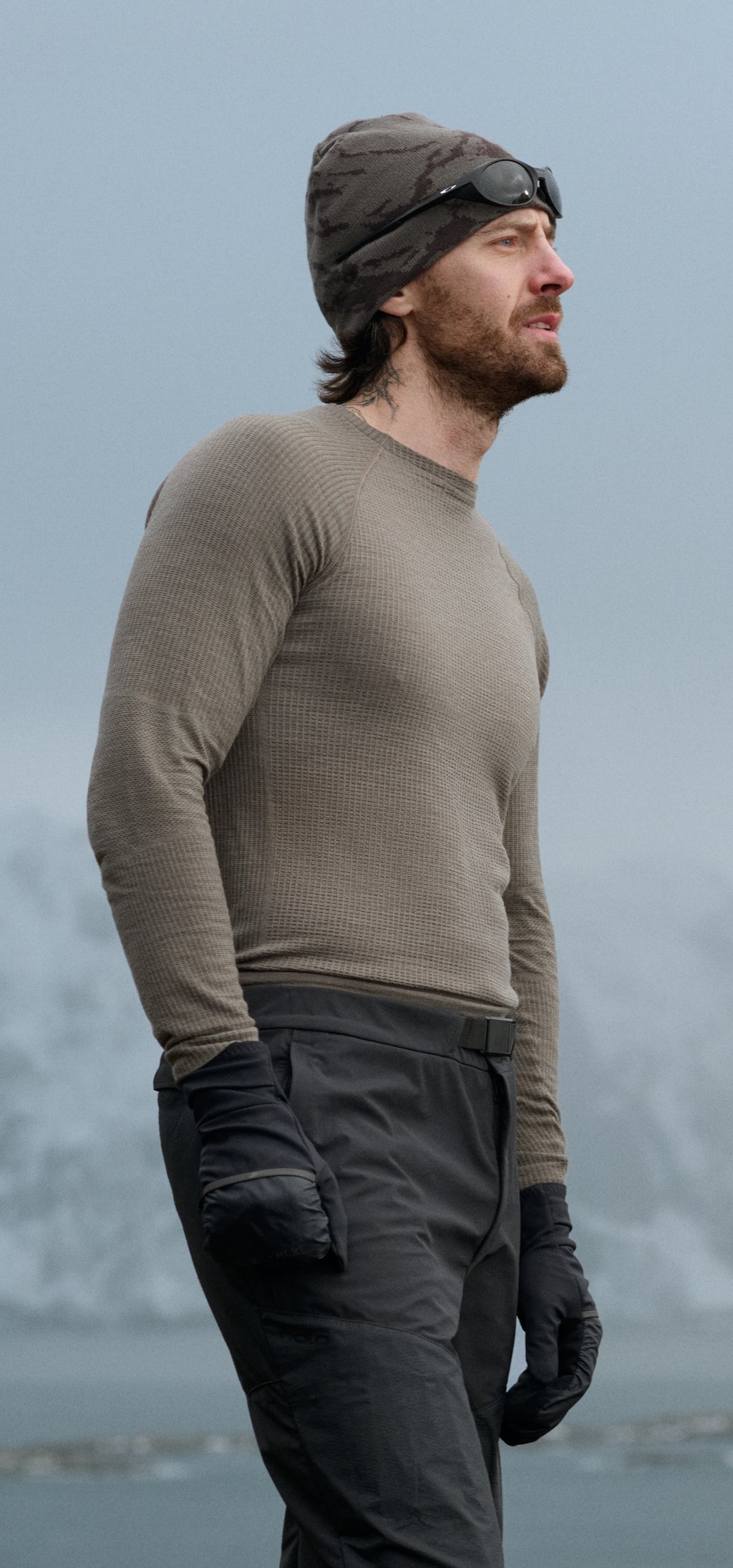Man and woman in base layers and beanies with sunglasses look into the distance against a foggy mountain backdrop.