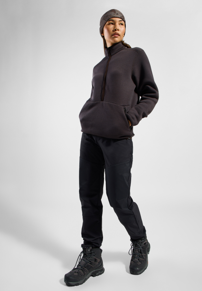 Person in a pale pink textured balaclava top, black outdoor trousers, and black hiking shoes against a white background.