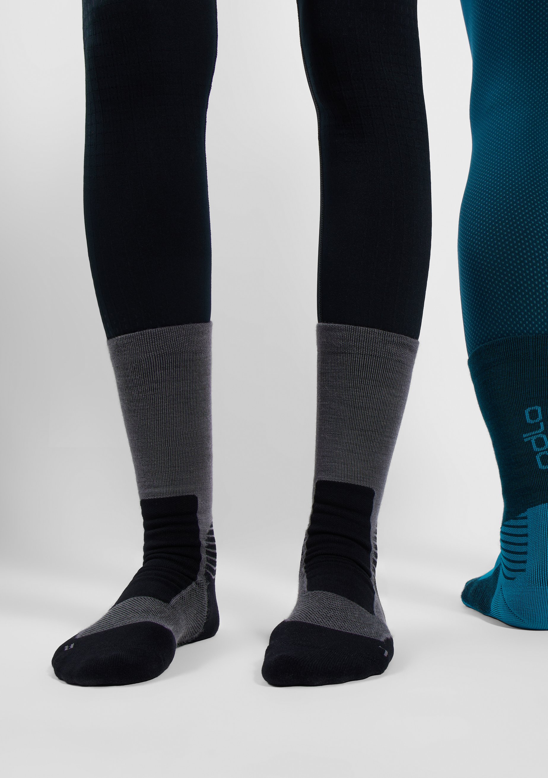 Person zieht pinke und violette knielange Kompressionssocken über eine helle Leggings auf weißem Hintergrund.
