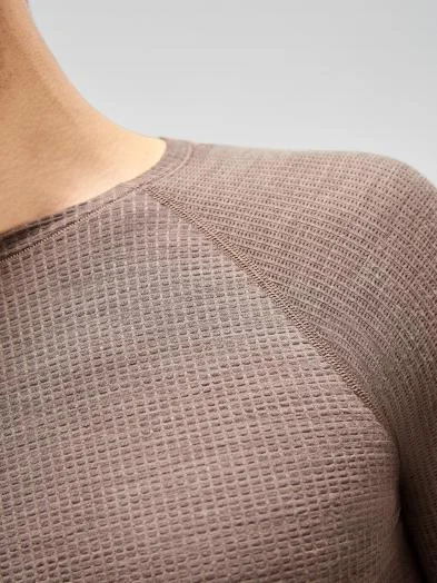 Close-up of a person's shoulder wearing a brown waffle-knit seamless performance wool base layer, highlighting the textured fabric and raglan seam detail.