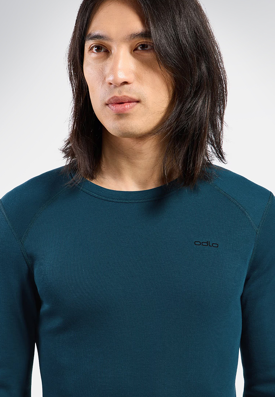 Person with long dark hair wearing a dark teal long-sleeved ribbed shirt with the Odlo logo on the chest.