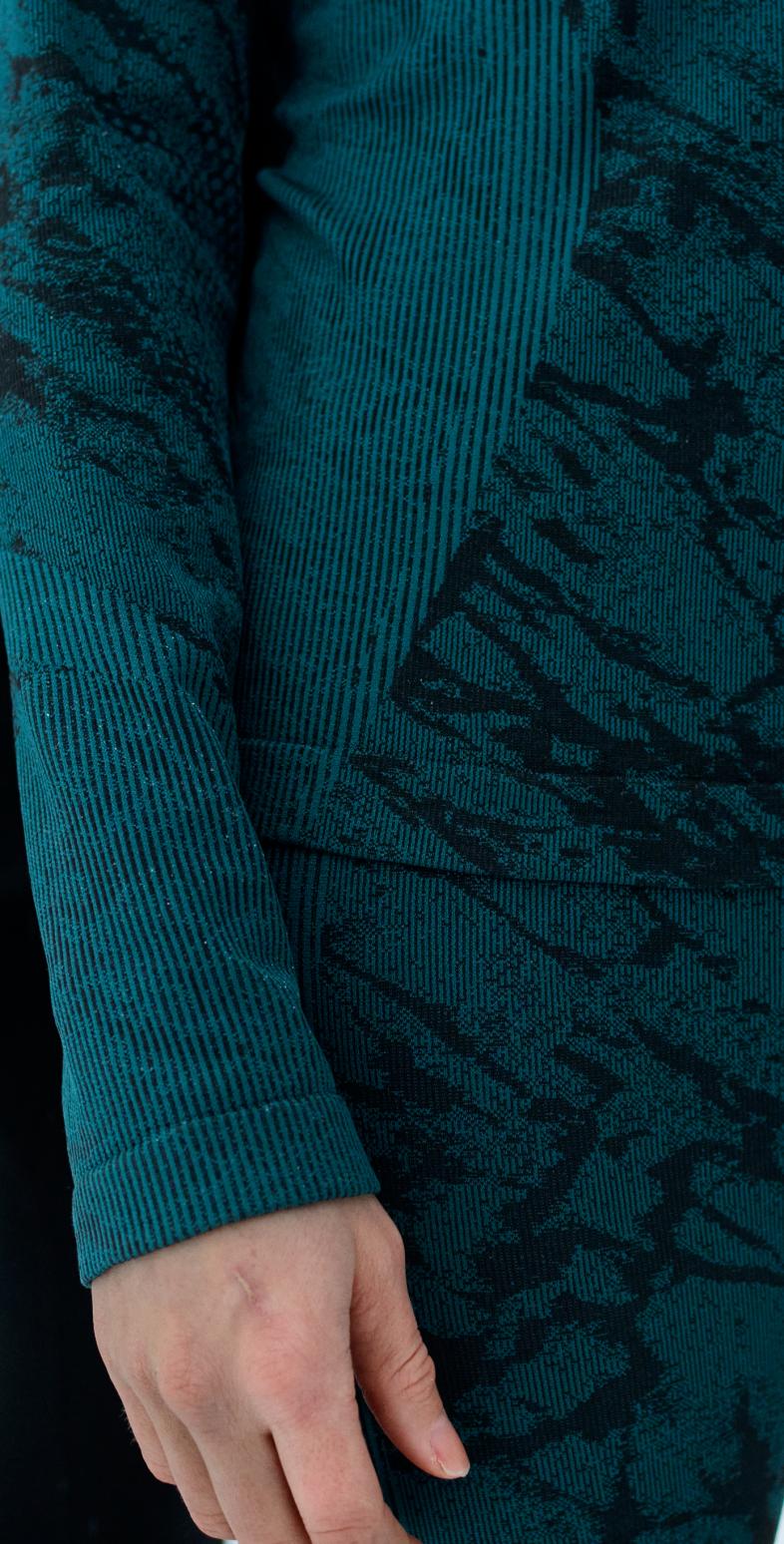 Close-up of two people in winter base layers: one in teal patterned top and leggings, the other in black, standing on snow with tattooed hand visible.