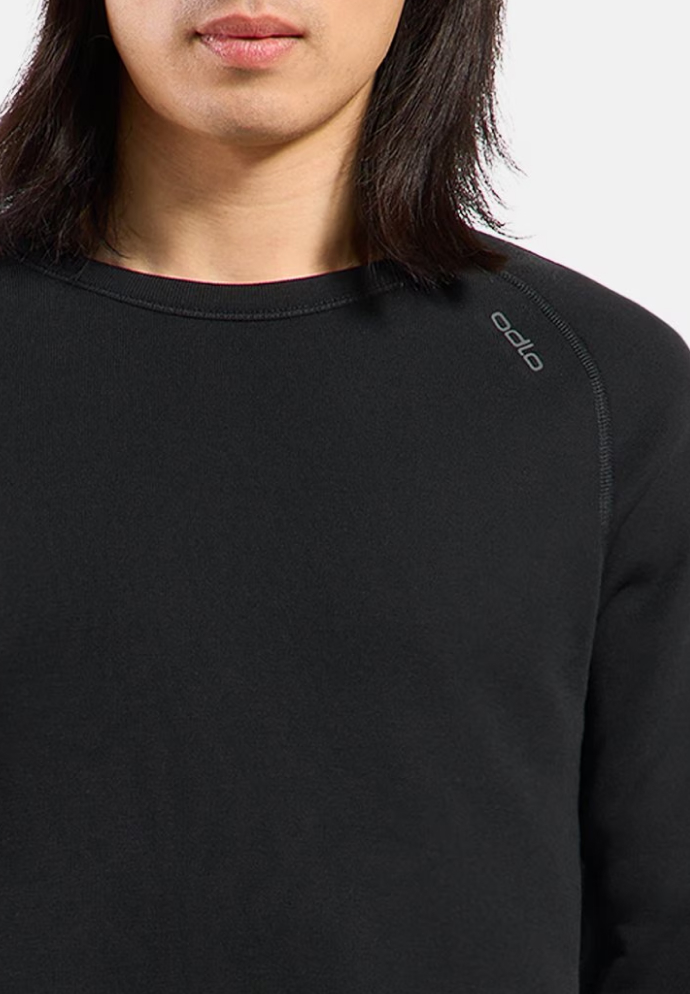 Nahaufnahme einer Person in einem schwarzen Base Layer Oberteil mit Rundhalsausschnitt und kleinem „odlo“-Logo auf der Schulter. Vor dem weißen Hintergrund sind lange dunkle Haare zu sehen.
