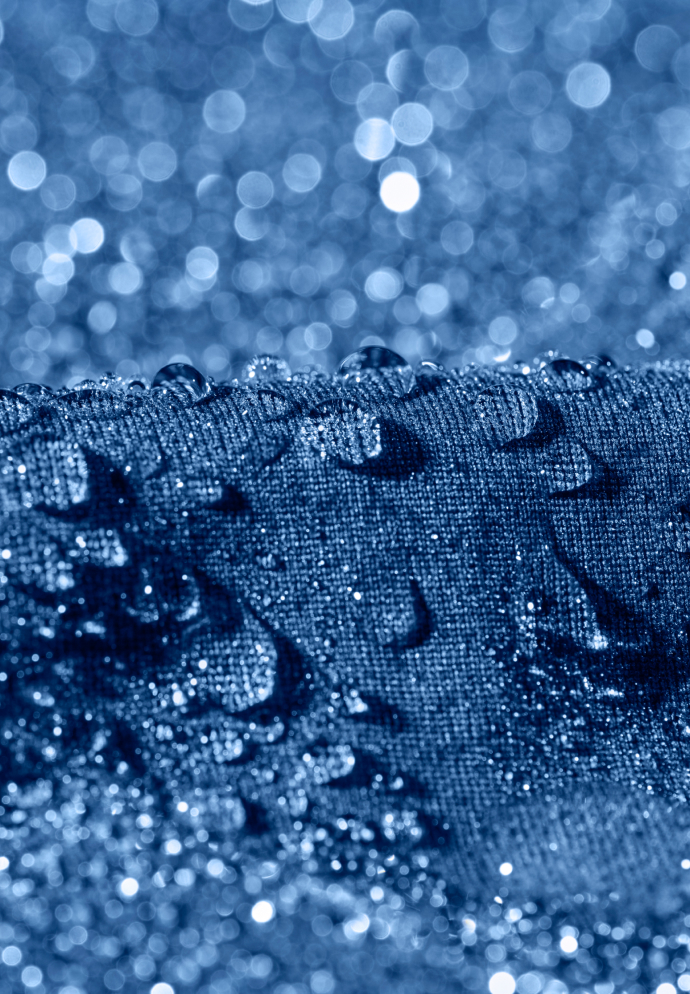 Close-up van heldere waterdruppels op donkerblauwe stof met textuur, met een glinsterende, vervaagde bokeh-achtergrond.
