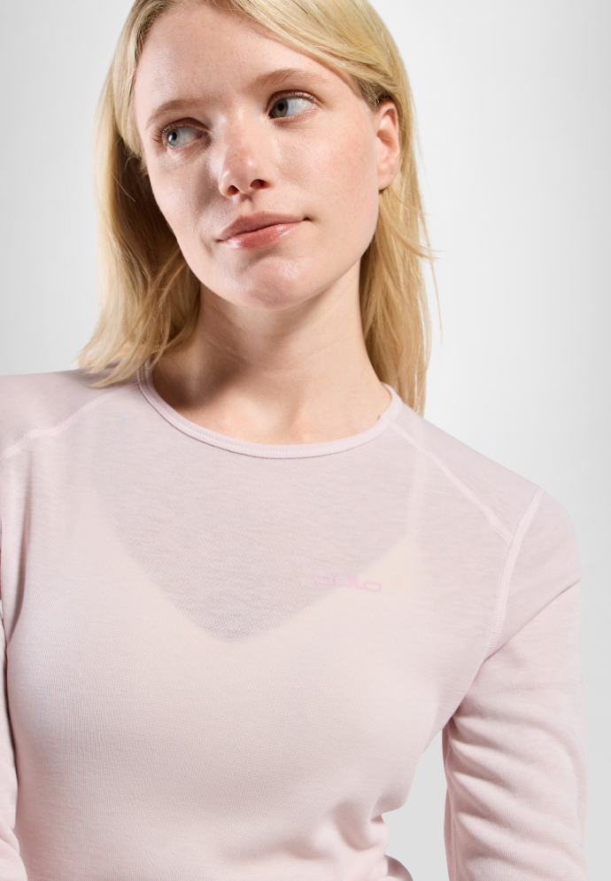 Vrouw met een donkerbruine merino midlayer met halve rits, een zwarte broek en een gepatroonde haarband, tegen een witte achtergrond.
