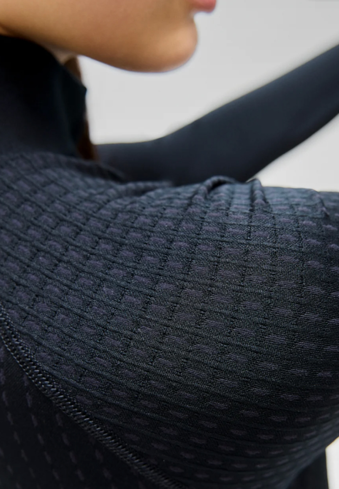 Nahaufnahme einer Frau in einem dunklen Base Layer Oberteil mit Struktur, die den gemusterten Schulterstoff und das Nahtdetail in weichem Licht zeigt.