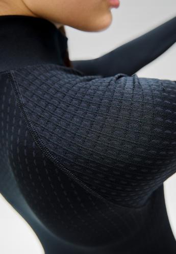 Close-up of a black, long-sleeved performance warm base layer on a person, showing textured grid and dotted mesh fabric patterns.