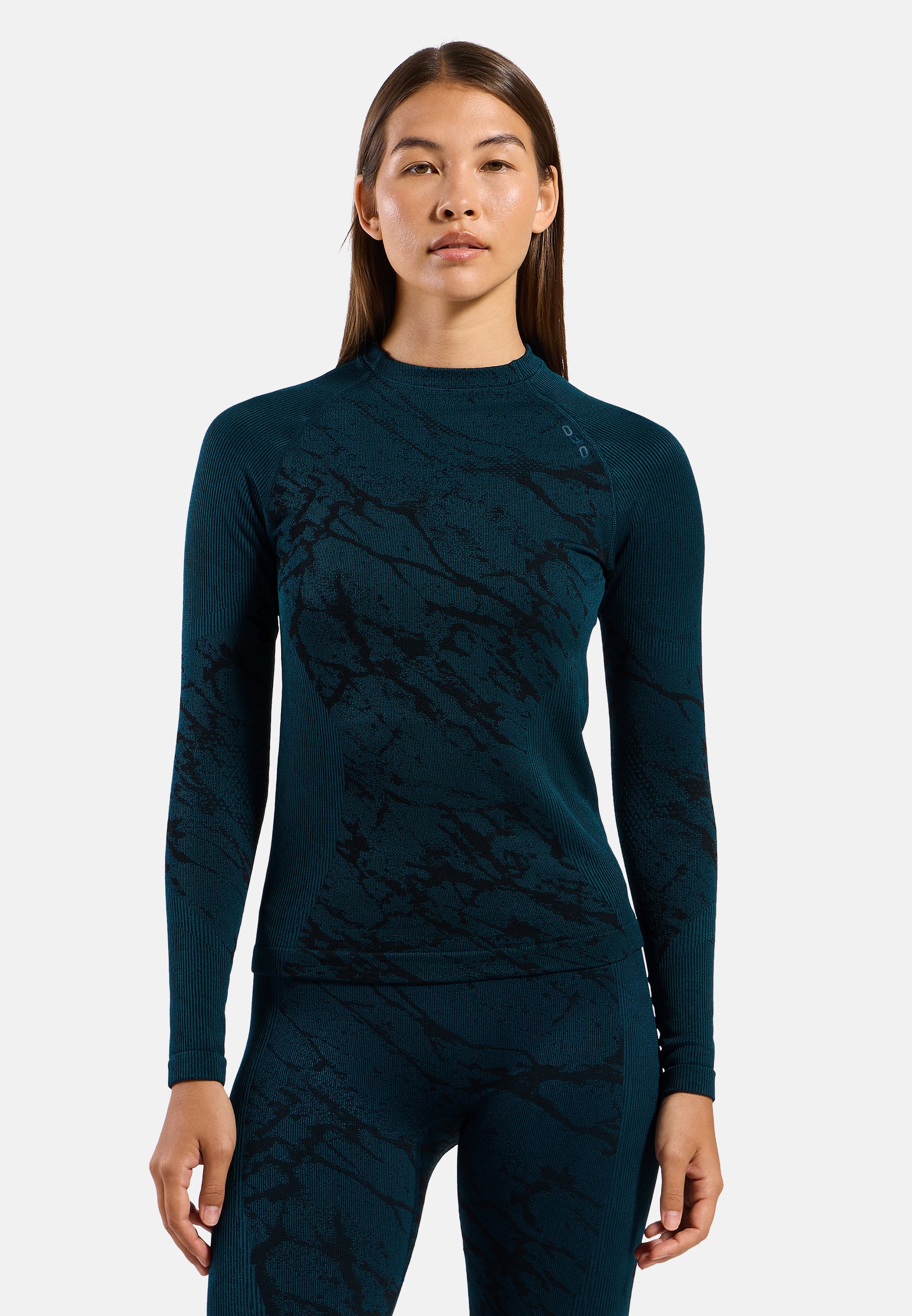 Woman wearing a fitted black long-sleeve athletic top and matching leggings, standing against a plain light grey background.