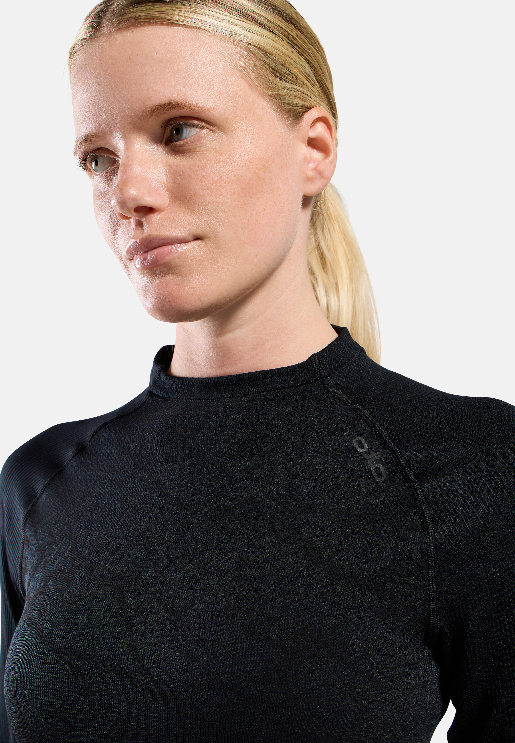 Close-up of a person wearing a teal, dotted long-sleeve performance base layer top, neutral expression, against a plain light background.
