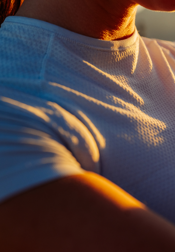 Close-up of a person's shoulder in a light base layer, highlighted by warm golden sunlight and deep shadows.