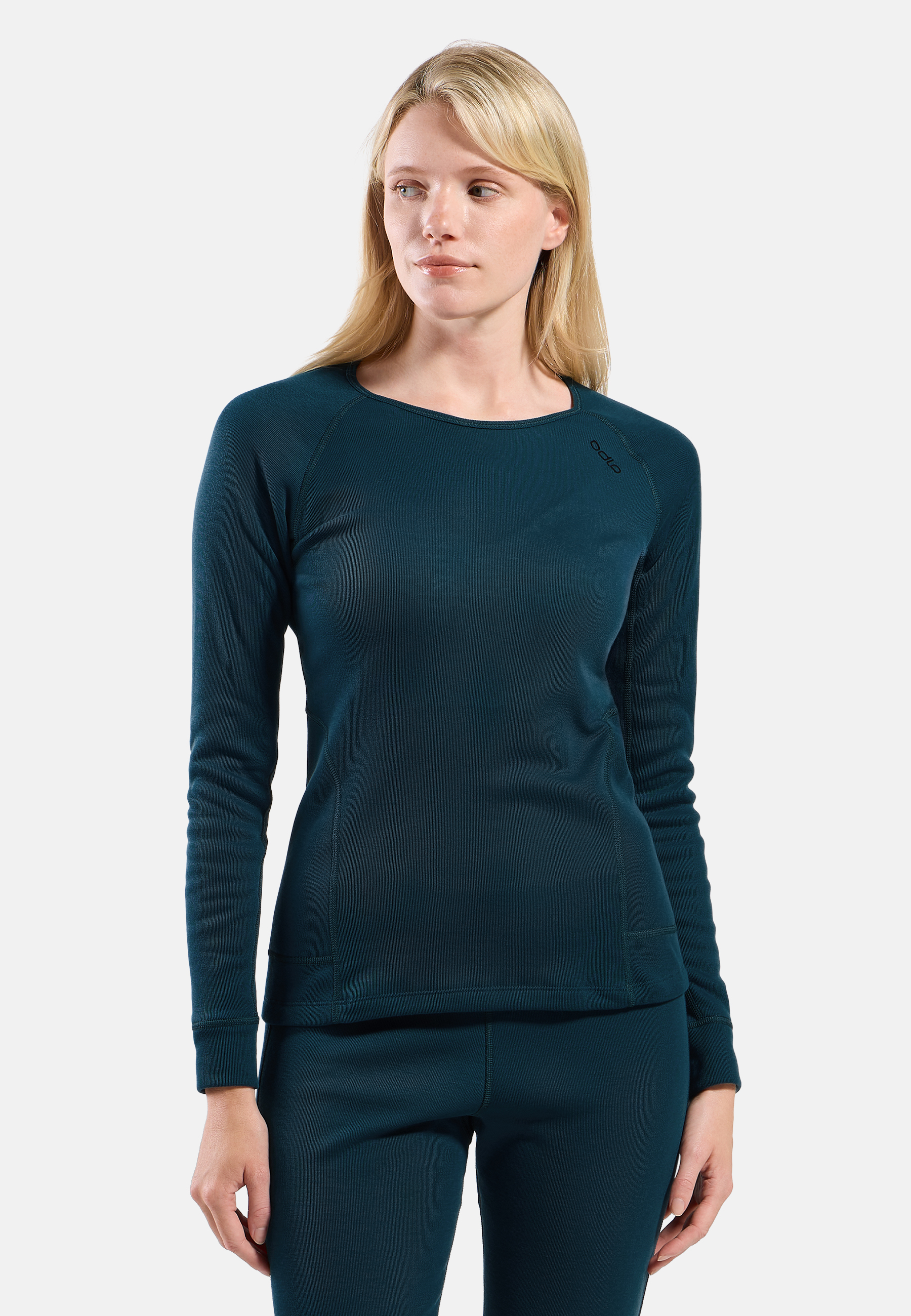 Woman modeling teal long-sleeve base layer top and matching leggings with subtle dotted pattern on a plain light grey background.