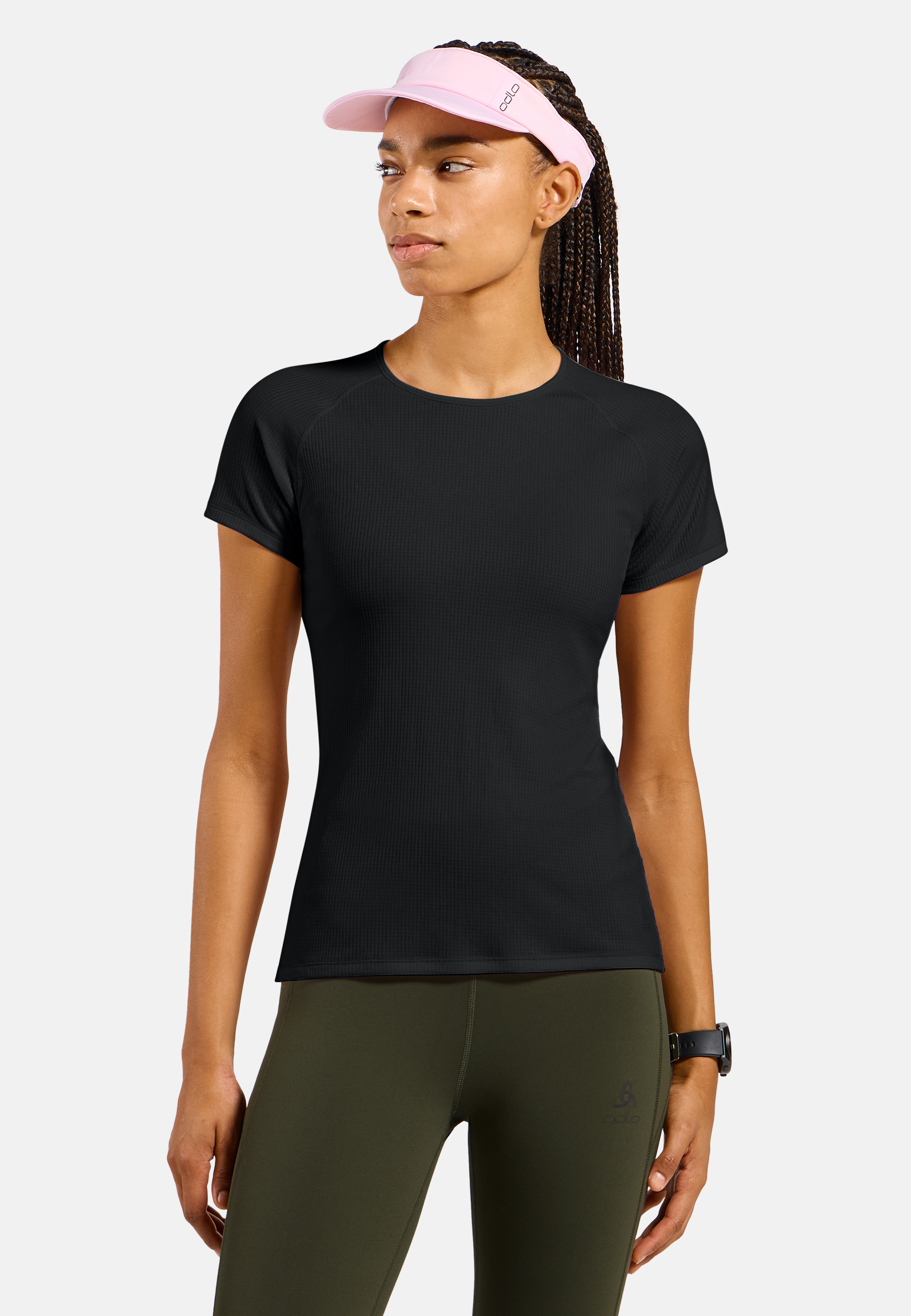 Athletic woman in black short-sleeve base layer top, olive leggings, and pink visor, looking left against a light grey background.