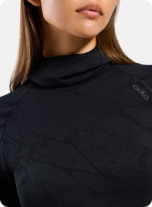 Close-up of a woman wearing a black mock-neck long-sleeve base layer top with subtle logo on the shoulder, against a light background.