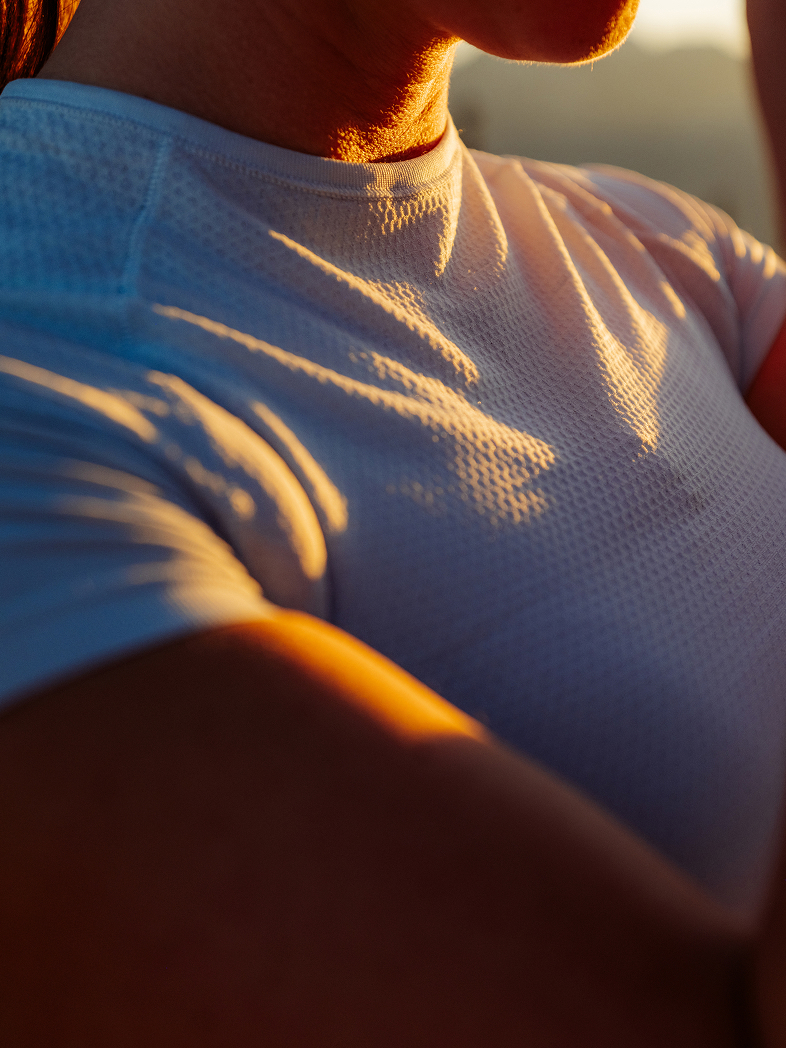 Close-up of a person wearing a white textured athletic base layer, illuminated by warm golden sunlight casting deep shadows.