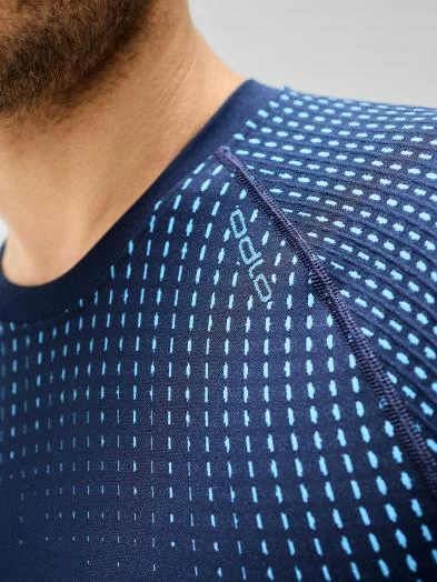 Close-up of a man wearing a dark blue performance warm base layer with a light blue dashed pattern, focusing on the shoulder seam.