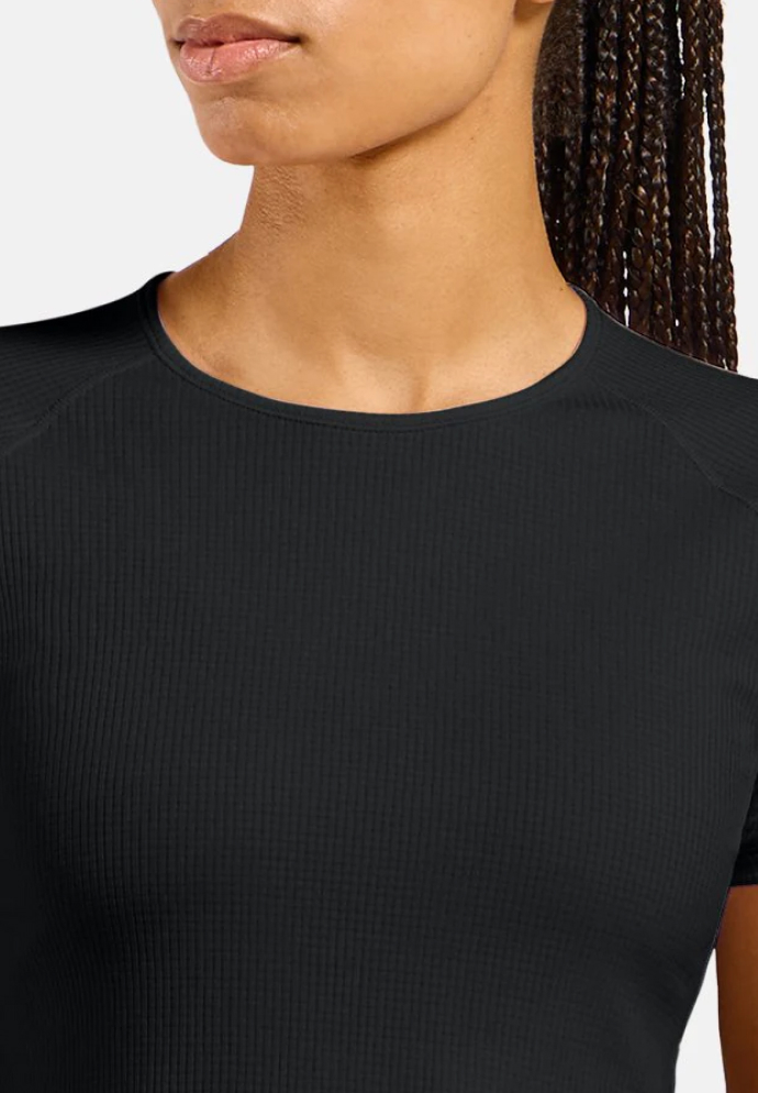 Nahaufnahme einer Person in einem eng anliegenden schwarzen Kurzarmshirt in Rippstrick mit Rundhalsausschnitt; seitlich sind geflochtene Haare zu sehen.