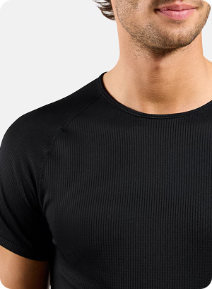 Close-up of a man wearing a fitted black ribbed short-sleeve base layer top, shown from chest to chin against a light grey background.