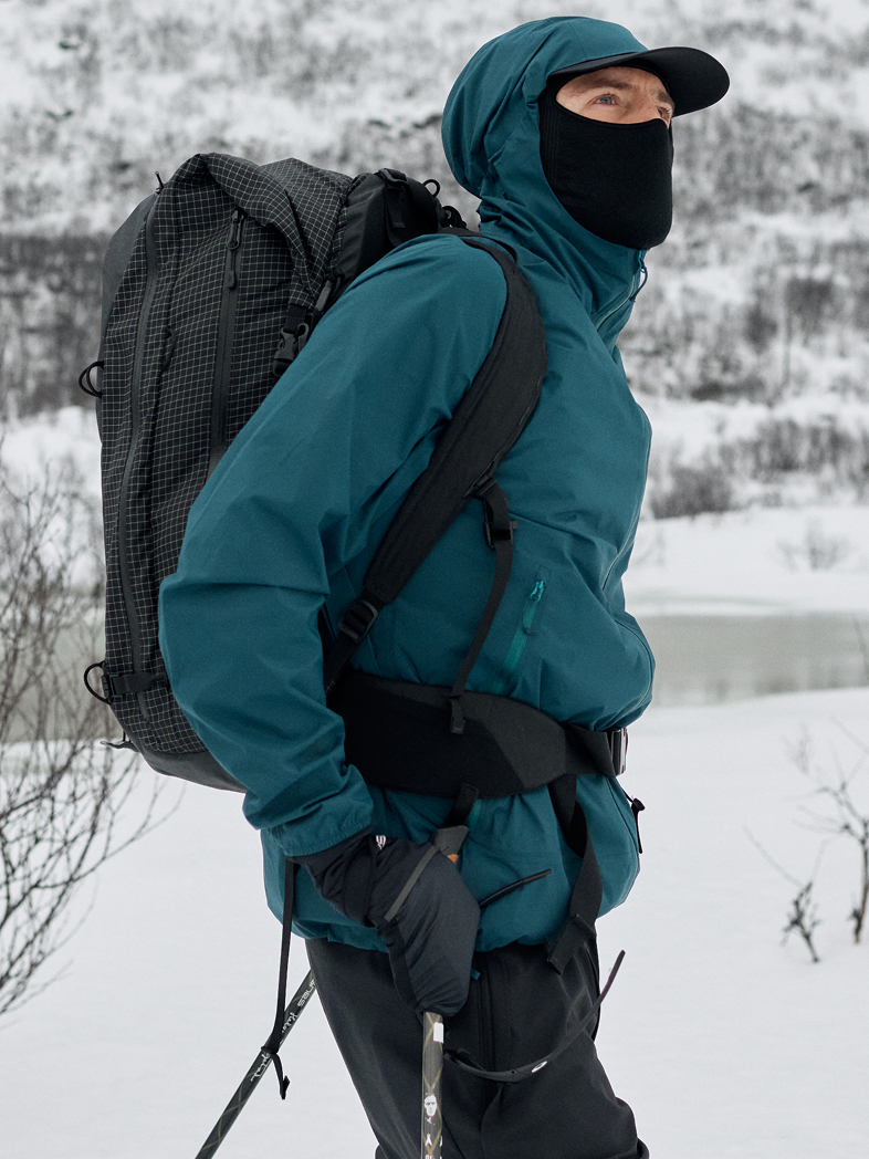 Two people in winter gear against a grey sky. A woman in a teal jacket stands in front of a bearded man in a dark jacket.