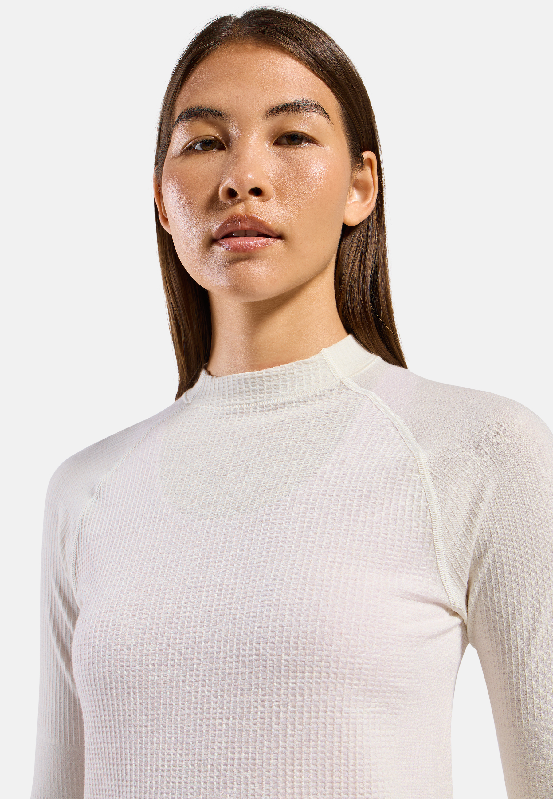Close-up of a woman wearing a textured off-white long-sleeve base layer top with a mock neck, against a plain light grey background.