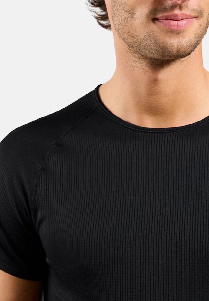 Close-up van de romp van een man in een getailleerd zwart geribbeld T-shirt met ronde hals, lichte stoppels zichtbaar, tegen een effen lichte achtergrond.