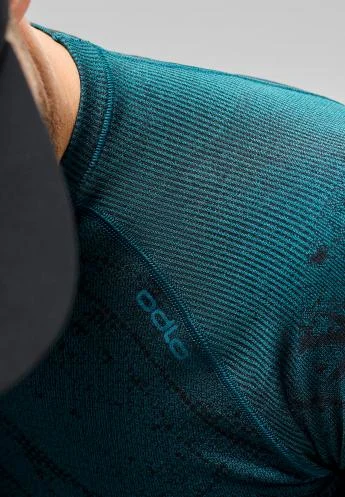Close-up of a dark teal, ribbed base layer on a men's shoulder, with a black cap partially visible.