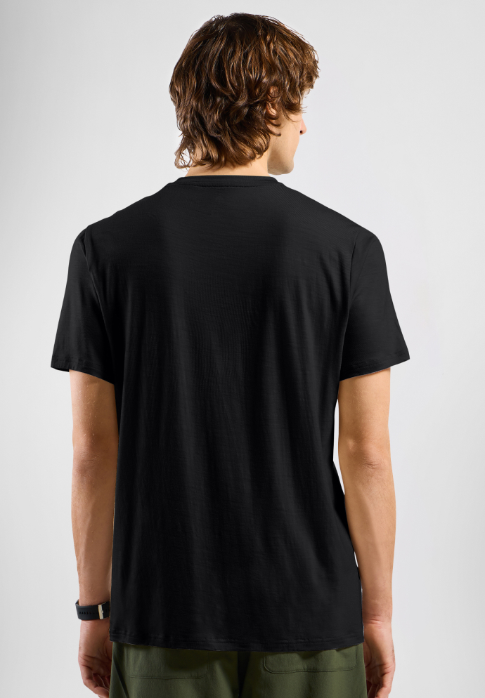 Achteraanzicht van een man met golvend bruin haar, gekleed in een effen zwart T-shirt met korte mouwen en een olijfgroene broek.