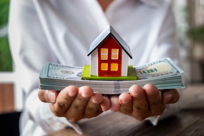 toy-house-resting-on-stack-of-money-in-hands.jpeg