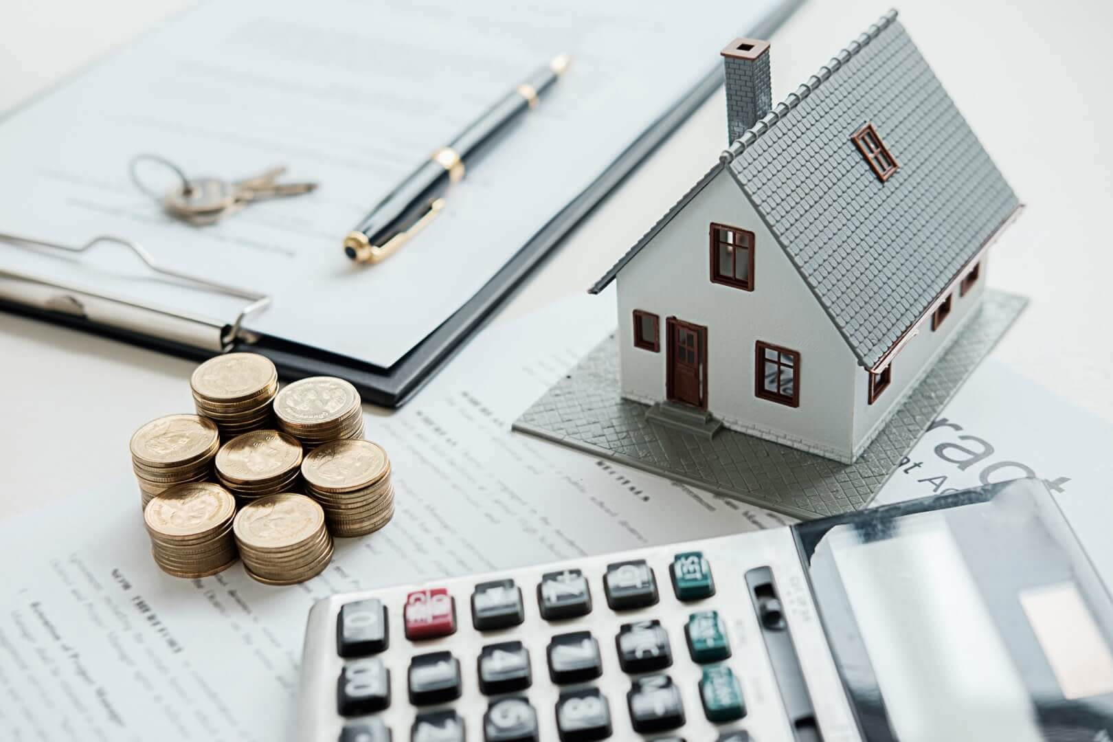 Image of a calculator, seven short stacks of quarters, a contract document, a pen, two keys on a keyring, and a tiny toy house.