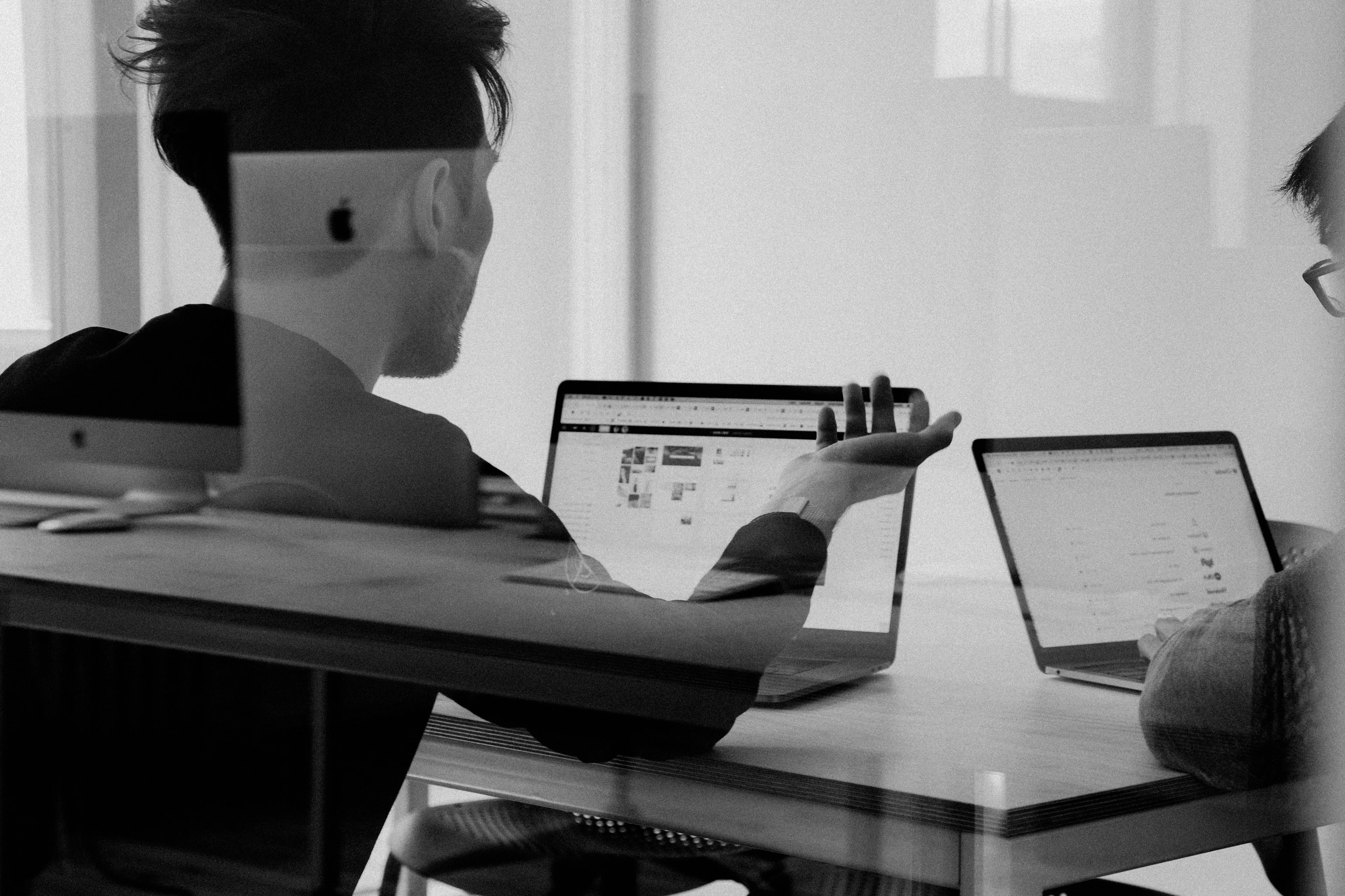 Två unga manliga utvecklare diskuterar sittandes vid ett bord med sina laptops framför sig.