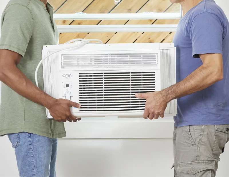 Two men place an AC unit in the window