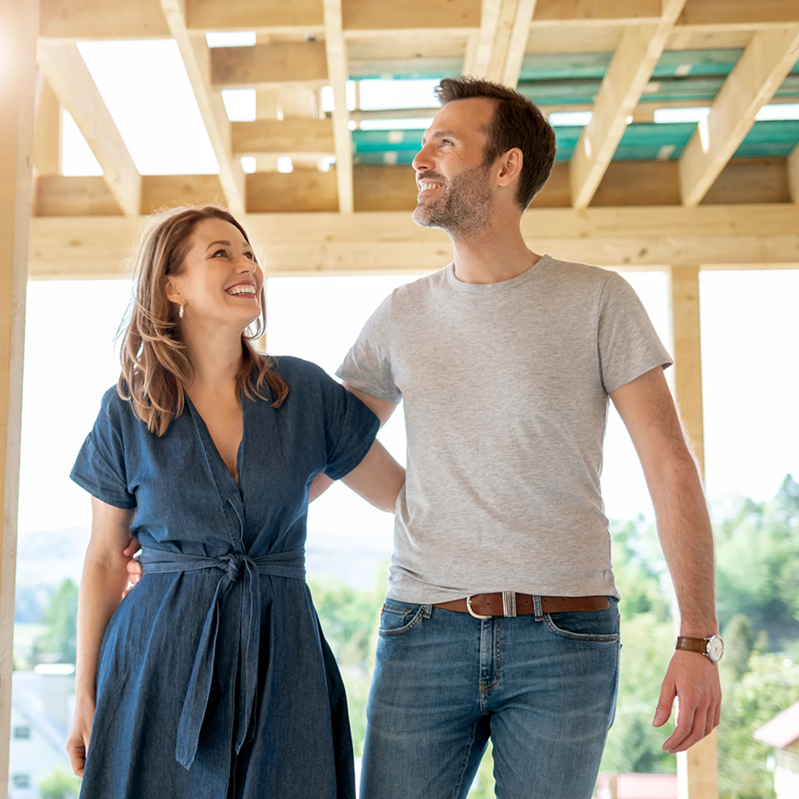 A happy couple stands inside the wooden frame of their new home. 